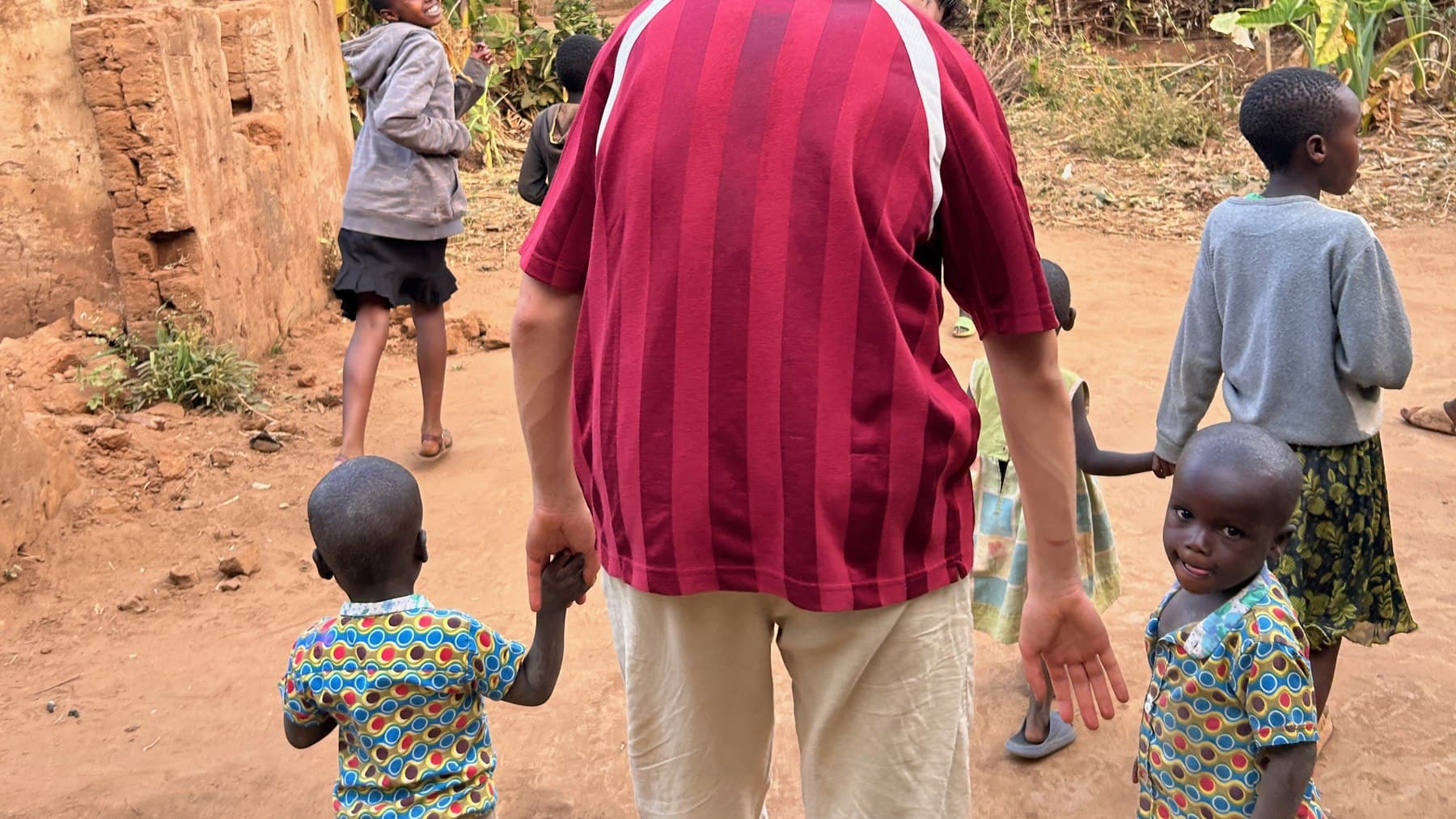 Un voluntario de la fundación camina de la mano con dos niños por un camino de Burundi